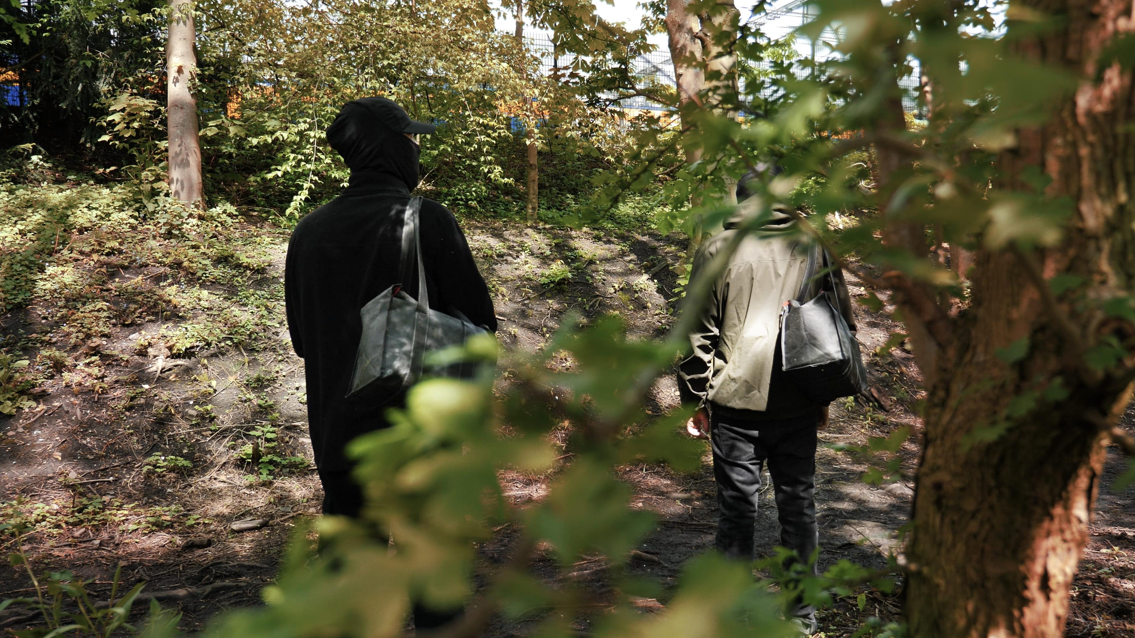 Two people in dark clothes walking through between trees