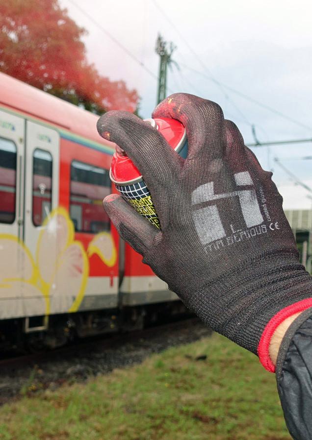 Closeup of a hand wearing a mr serious glove while spray painting a red color. In the background a german train can be seen